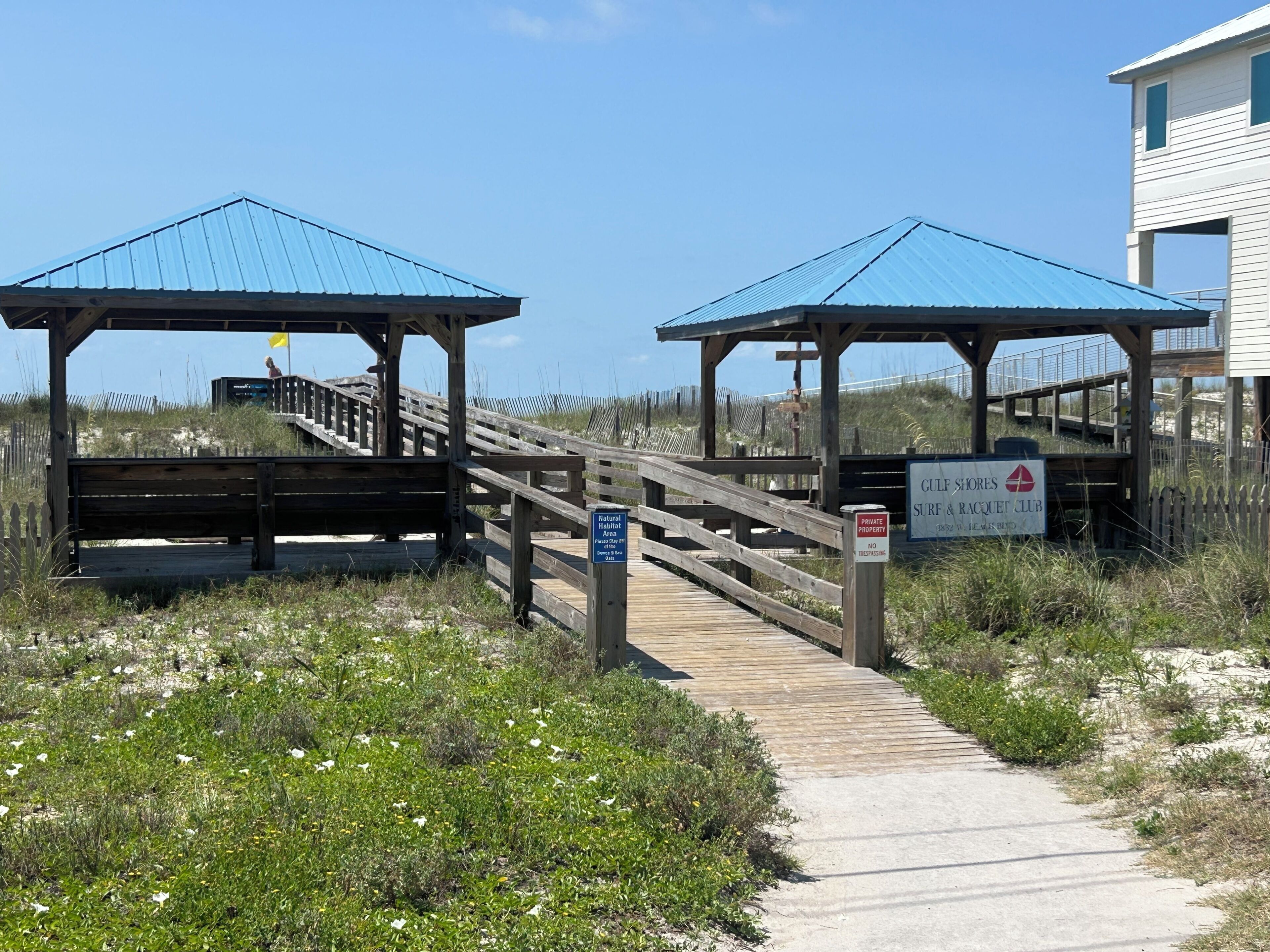 A wooden boardwalk leading to beach huts with a sign indicating private property and no trespassing.