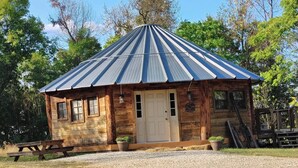 A rustic wooden cabin with a metal roof, a front door, and two windows. - The Highlander Rustic Yurt (Genoa)