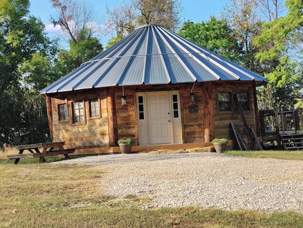 A rustic wooden cabin with a metal roof, a front door, and two windows. - The Highlander Rustic Yurt (Genoa)