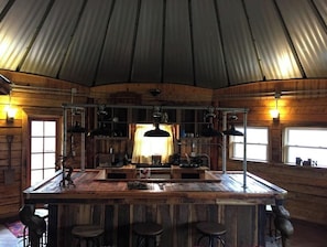 A rustic wooden interior with a central bar area, bar stools, and pendant lighting. - The Highlander Rustic Yurt (Genoa)
