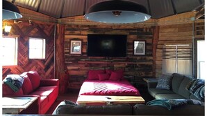 A cozy cabin interior with a large bed, a sofa, and a television mounted on the wall. - The Highlander Rustic Yurt (Genoa)
