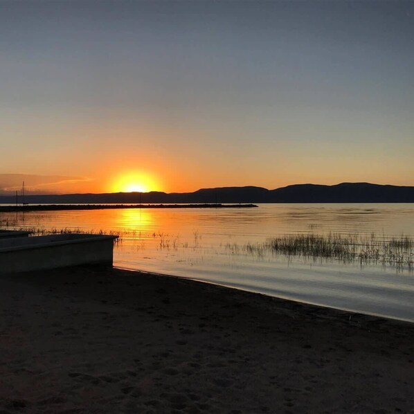 A calm lake at sunset with a boat on the shore and distant hills.