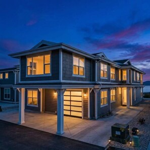 A two-story residential building with a garage, a covered front porch, and a view of the water.