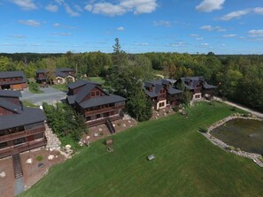 A cluster of log cabins with a grassy lawn and a small pond.