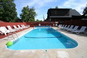 A rectangular pool with a 'NO DIVING' sign, surrounded by white lounge chairs, a ladder, and a red fence.