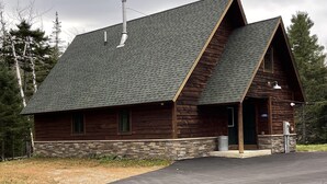 Eine Blockhütte mit Stein Fundament, einem steilen Satteldach und einer Veranda.