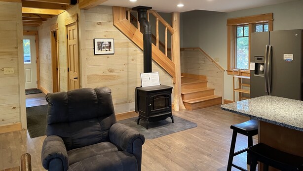 Ein gemütliches Interieur mit einer Holztreppe, einem schwarzen Polsterstuhl, einem Holzofen und einem Edelstahl-Kühlschrank.