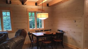 Ein gemütliches Blockhaushaus-Interieur mit einem Holzesstisch, Stühlen, einer Couch und einem Fenster mit Blick auf Bäume.