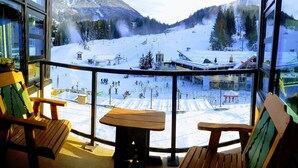 A snow-covered ski slope with a chairlift and buildings in the background.