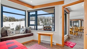 A cozy room with a large window overlooking a snowy landscape, a wooden bench with cushions, and a small table.