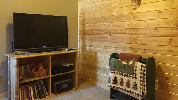 A room with a television on a wooden stand, a bookshelf, and a blanket draped over a chair.