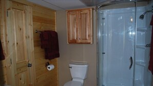 A bathroom with wooden walls, a toilet, a glass shower enclosure, and wooden cabinets.