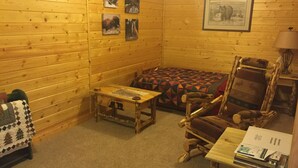 A cozy cabin interior with wooden walls, a quilted sofa, a wooden table with a map, and a framed picture on the wall.