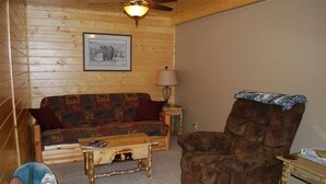 A cozy room with a wooden wall, a framed picture, a sofa, a chair, a lamp, and a small table.