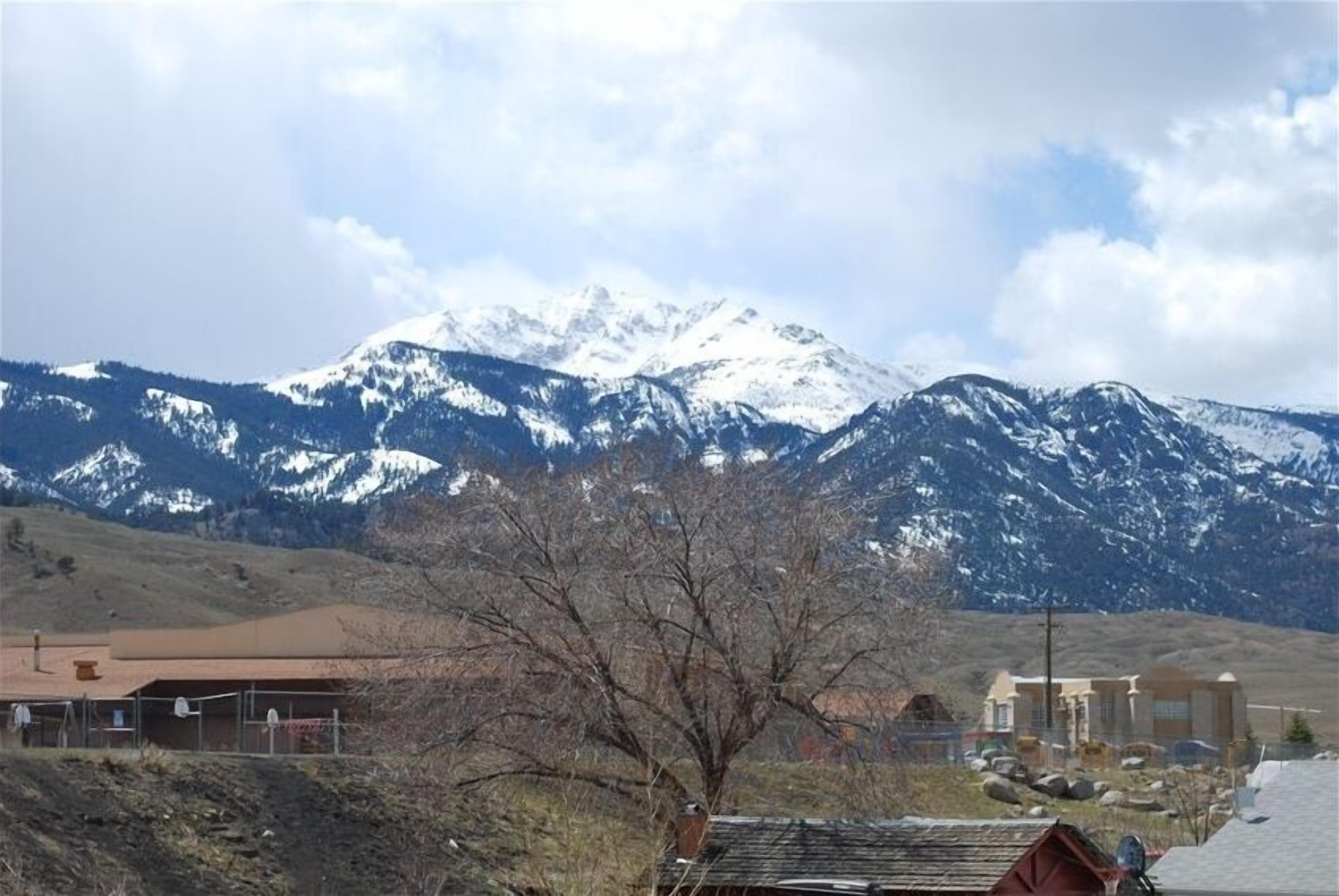 A mountain with snow-capped peaks in the background, a building with a red roof in the foreground, and a clear sky.