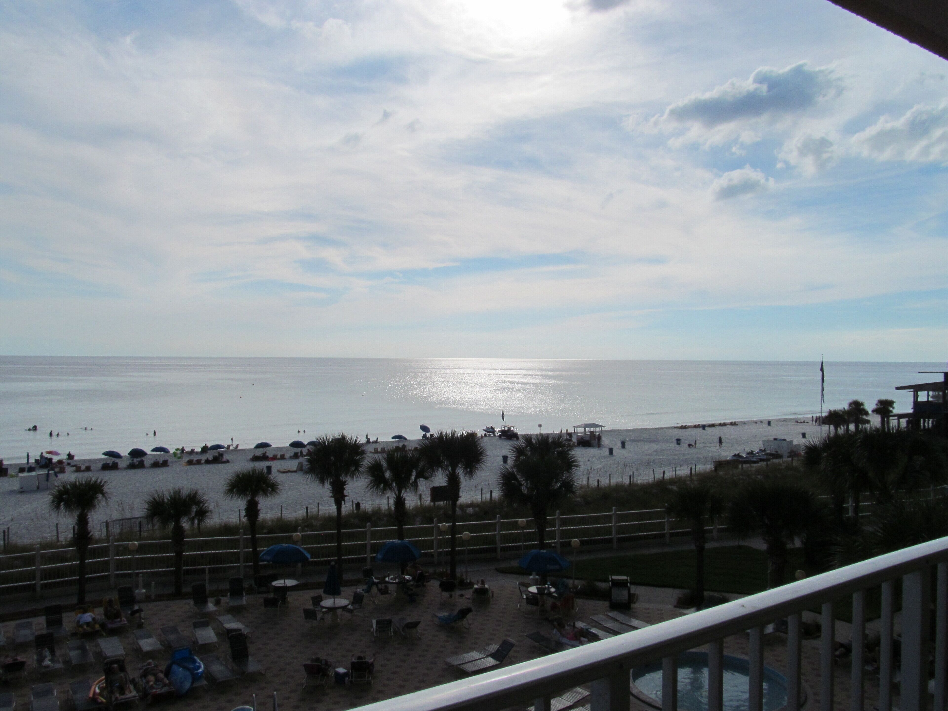 Vista da praia com guarda-sóis, espreguiçadeiras e piscina.