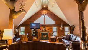 A cozy cabin interior with a fireplace, leather furniture, and mounted animal heads. - Country Getaway Lodge/Ranch near Saratoga Springs (valley Falls)