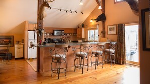 A kitchen with wooden cabinets, a bar area with stools, and antlers mounted on the ceiling. - Country Getaway Lodge/Ranch near Saratoga Springs (valley Falls)