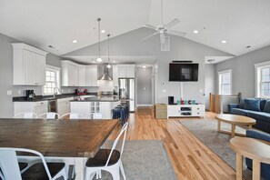 Een moderne keuken met witte kasten, een eethoek met een houten tafel, en een woonkamer met een blauwe bank.