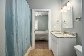 Een badkamer met een douche, een wastafel met een marmeren aanrechtblad, een toilet en een plafondventilator.