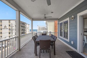 Een balkon met een tafel en stoelen, een plafondventilator, en uitzicht op het strand en gebouwen.