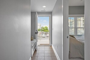 A narrow hallway with a door leading to a balcony with a view of buildings and trees.