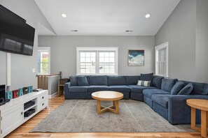 A modern living room with a sectional sofa, a flat-screen TV, and a fireplace. - 7 Bedroom, Oceanview House, Steps from Boardwalk! (Ocean City)