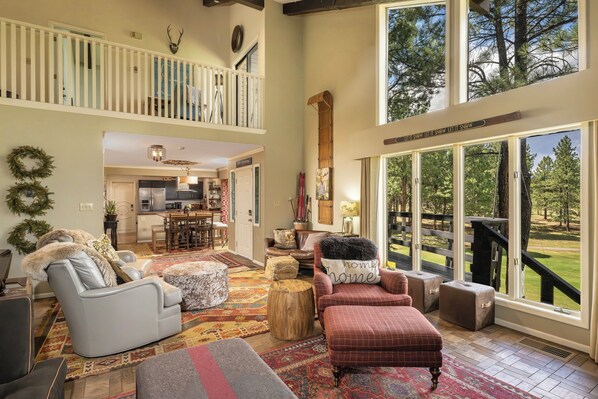 A spacious living area with a high ceiling, a dining area, and a view of a landscaped outdoor area.