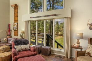 A cozy living room with a large window, a wooden door, and a view of a deck and trees.