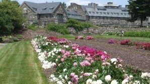 A large stone building with multiple chimneys and a well-maintained garden with pink and white flowers. - 7BR Pocono home on Skytop property+ access to many resort activities/golf/dining (Skytop)