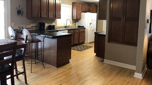 A kitchen with wooden cabinets, a refrigerator, a coffee maker, and a dining area with chairs and a table.