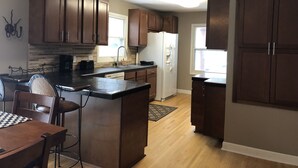 A modern kitchen with wooden cabinets, a central island, a dining area with a table and chairs, and a refrigerator.