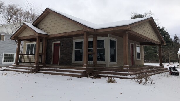 A two-story house with a covered porch and a snow-covered roof.