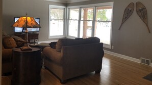 A living room with a sofa, a lamp, a television, and large windows.