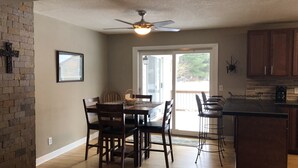 A dining area with a wooden table and chairs, a ceiling fan, and a view through a glass door to an outdoor deck.