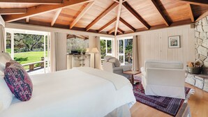 Une chambre avec un grand lit, un coin salon comprenant un fauteuil et une table, et un mur en pierre.