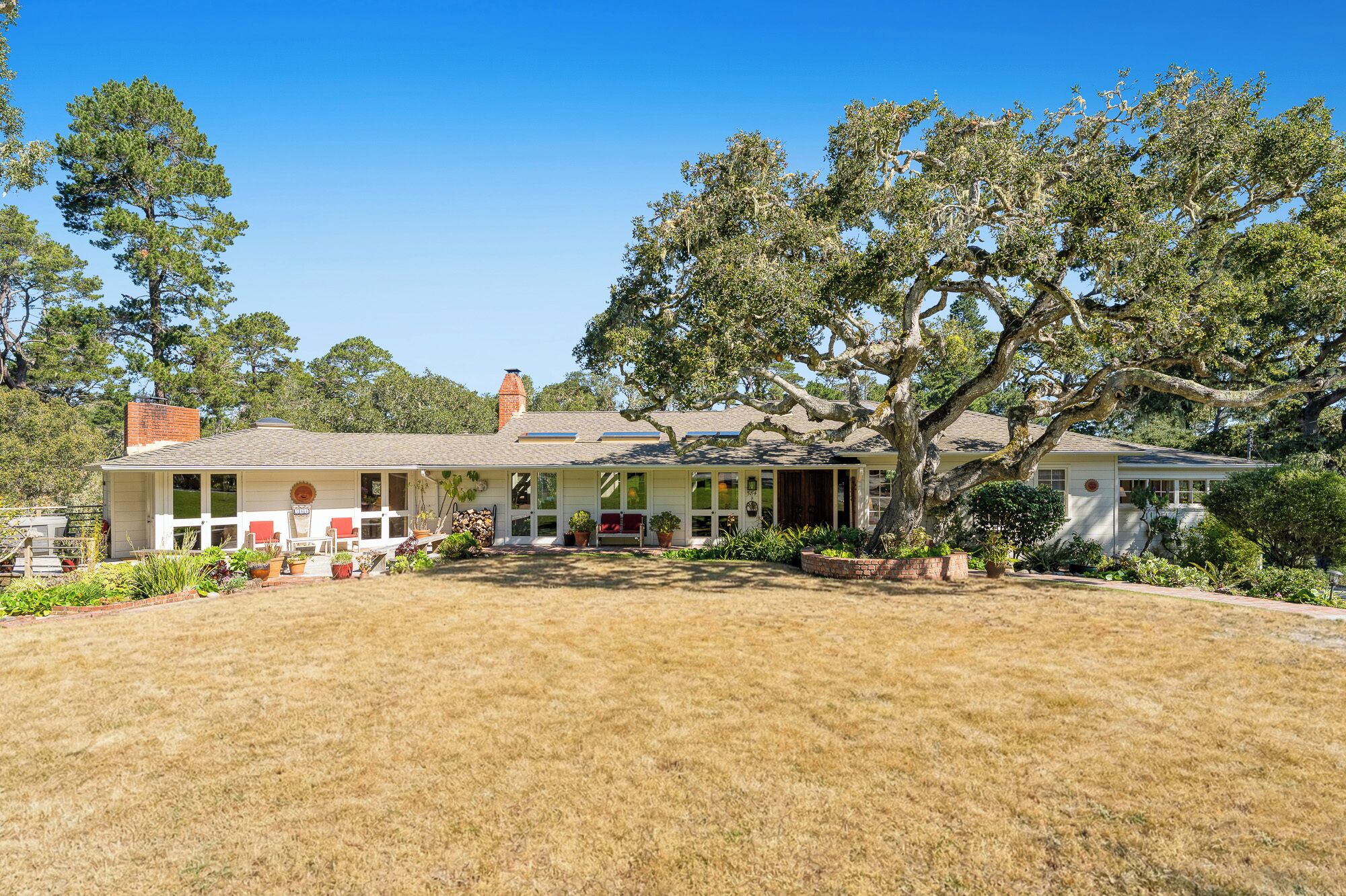 A two-story house with a front porch, a brick chimney, and a large tree in the front yard.