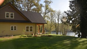 Una casa de dos pisos con un porche, una pequeña terraza y vista a un lago.
