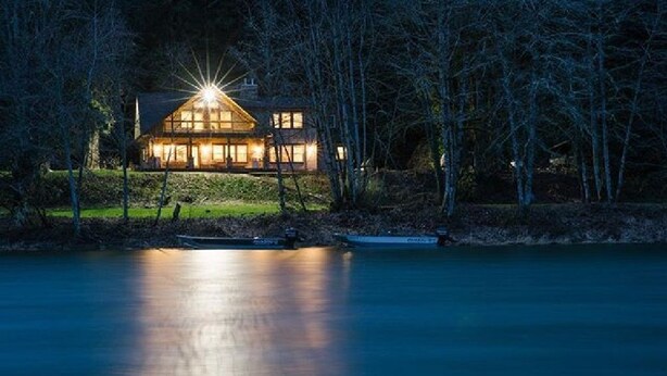 Una casa junto a un lago de noche, con un barco amarrado al frente.
