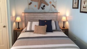 A bedroom with a bed, two bedside lamps, a starfish wall decoration, and framed pictures on the wall. - Cozy Riverside Studio Condo Two Minute Walk To Wells Beach
 (Wells)
