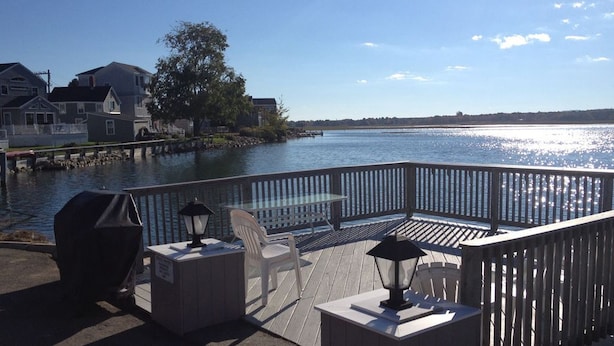 A deck with a table and chairs overlooking a calm body of water, with houses in the background. - Cozy Riverside Studio Condo Two Minute Walk To Wells Beach
 (Wells)