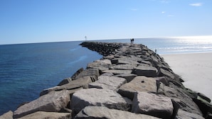 A rocky breakwater extending into the sea with a lighthouse in the distance. - Cozy Riverside Studio Condo Two Minute Walk To Wells Beach
 (Wells)