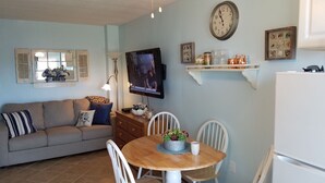 A living room with a sofa, a dining table with chairs, a television, and decorative items on the wall. - Cozy Riverside Studio Condo Two Minute Walk To Wells Beach
 (Wells)