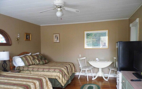 A bedroom with two beds, a ceiling fan, a TV, a small table with a chair, and a painting on the wall. - Room 3 at Otter Creek Inn (Mt Desert)