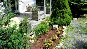 A garden with a wooden deck, potted plants, and a variety of shrubs and flowers. - Room 3 at Otter Creek Inn (Mt Desert)