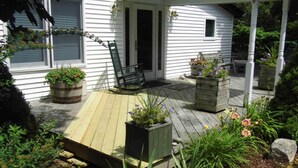 A wooden deck with a bench and planters, a porch with a door, and a small window. - Room 3 at Otter Creek Inn (Mt Desert)