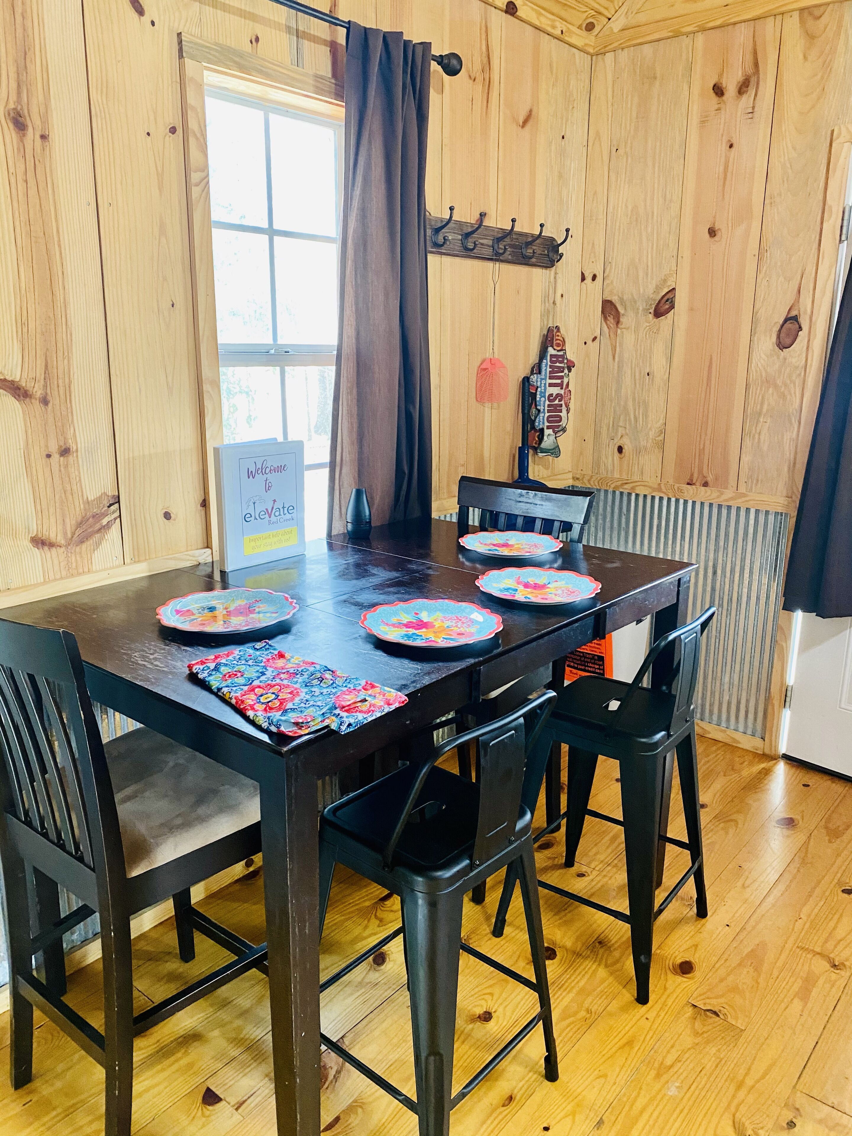 A wooden-paneled room with a dining table set for four, featuring colorful placemats and black chairs.