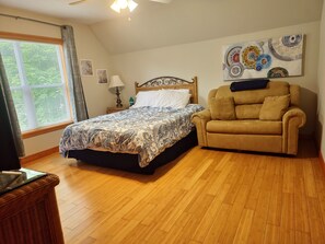 Une chambre à coucher comprenant un lit, un canapé, une fenêtre avec des rideaux, un ventilateur de plafond et un tableau mural.