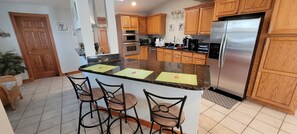 A kitchen with wooden cabinets, a stainless steel refrigerator, and a central island with bar stools. - SPACIOUS SoHa FAMILY RETREAT! Walk to Town! Mins to Beach! Sleeps 12! Large Lot! (South Haven)