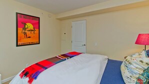 A hotel room with a bed, a poster on the wall, a door, and a lamp. - OCEAN VIEWS!!!! Penthouse located across the street to beach!! (Oceanside)